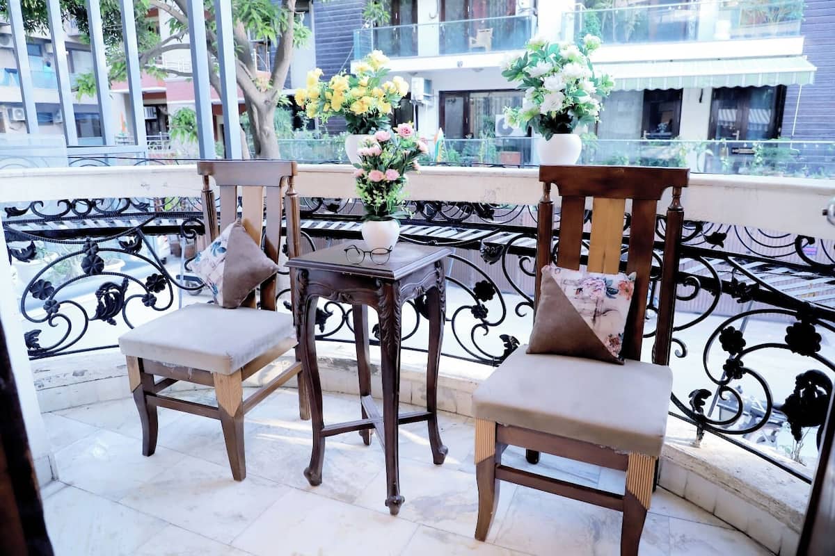 Een balkon met twee houten stoelen, een tafeltje en een bloevas.