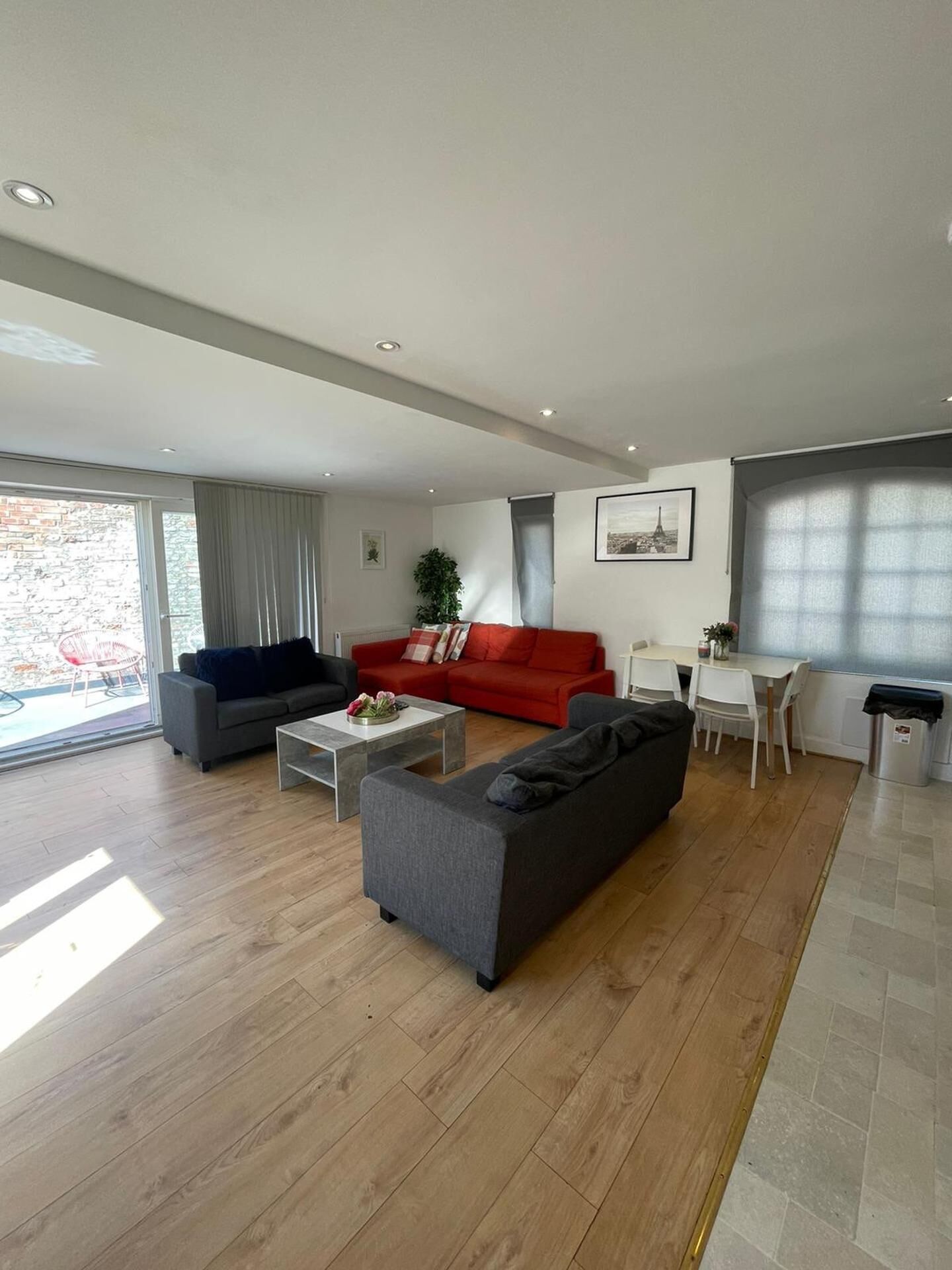 A modern living room with a grey sofa, a red sofa, a coffee table, and a dining area with chairs and a table.