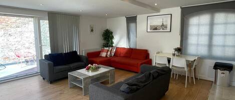 A modern living room with a grey sofa, a red sofa, a coffee table, and a dining area with chairs and a table.