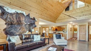 Un vaste espace de vie agrémenté d’un grand plafond en bois, d’un canapé en cuir, d’un fauteuil blanc et d’une œuvre d’art murale au style rustique.