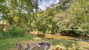 Un terrain de camping situé au bord de la rivière, équipé de deux fauteuils Adirondack en bois et d’un foyer.