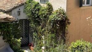 A narrow alley with buildings on either side, a window with shutters, and a small garden area with plants and a statue. - Madama Lucrezia - Fontana di Trevi (Rome)