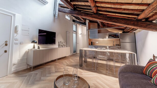 A modern kitchen with a dining area, wooden flooring, and a TV mounted on the wall. - Madama Lucrezia - Fontana di Trevi (Rome)