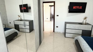 A modern bedroom with a large mirror, two beds, a dresser, and two TVs mounted on the wall. - Stabia Apartment (Angri)