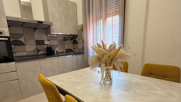 A modern kitchen with a dining area, including a table with chairs and a vase of dried plants. - Stabia Apartment (Angri)