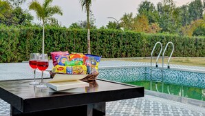 Ein Tisch am Pool mit Snacks, Getränken und einem Buch, umgeben von Wasser und Pflanzen.