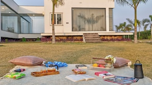 Ein modernes Haus mit Glasfassade, einer Beton-Terrasse mit Picknickmöbeln und Palmen.