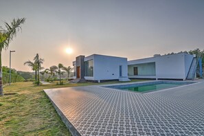 A modern building with a swimming pool, surrounded by a landscaped garden and a patterned patio.