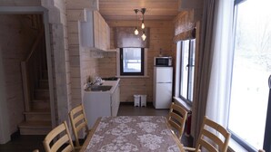Un intérieur en bois comprenant une table à manger, des chaises, un coin cuisine avec un four à micro-ondes et un réfrigérateur, ainsi qu’une fenêtre.