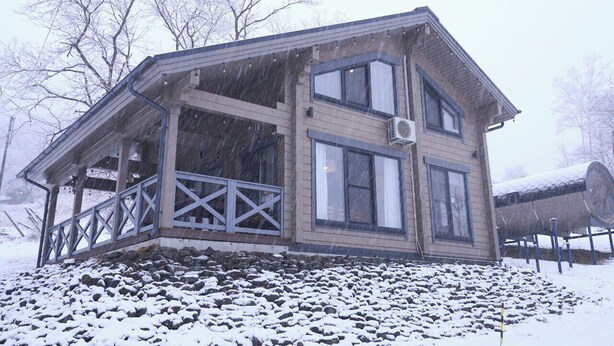 Une maison en bois à deux étages, dotée d’un balcon, entourée d’un paysage enneigé.
