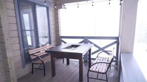 Une terrasse en bois avec une table et deux bancs, une fenêtre et des guirlandes lumineuses.