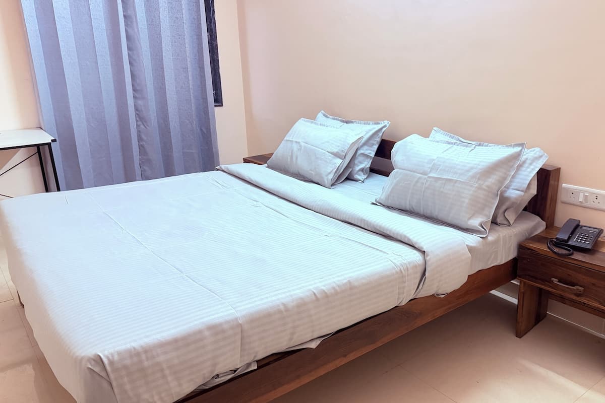 Un lit simple avec un cadre en bois, une table de chevet avec un téléphone et une prise électrique au mur.