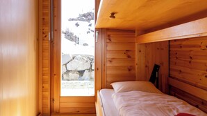 A wooden room with a bed, a door leading outside, and a stone wall. - Hauts de Nendaz E by Interhome (Nendaz)