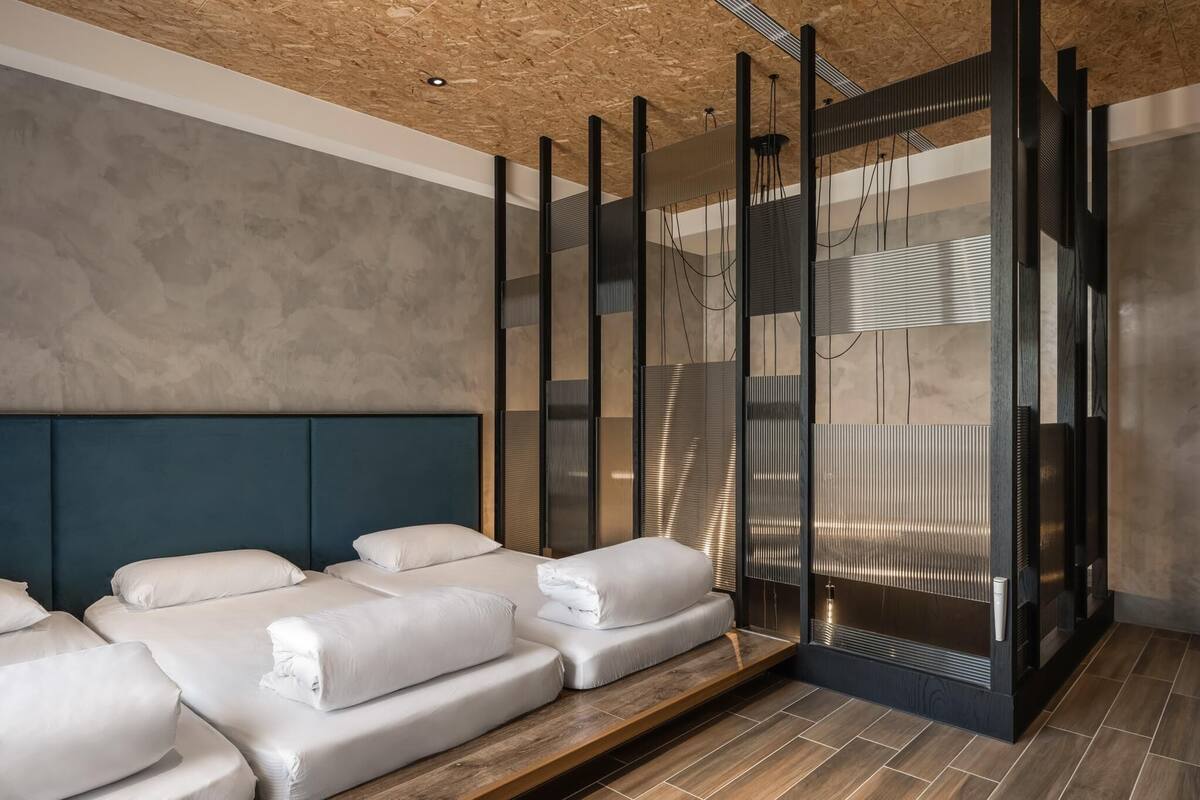 Quarto de hotel moderno com uma cama grande, mesa de massagem e teto de madeira.