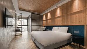 A modern bedroom with a large bed, wooden panel walls, and a herringbone floor pattern.