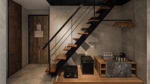 Una escalera moderna con escalones de madera y barandillas de metal, una puerta de madera y una pequeña mesa con botellas de agua y una cafetera.