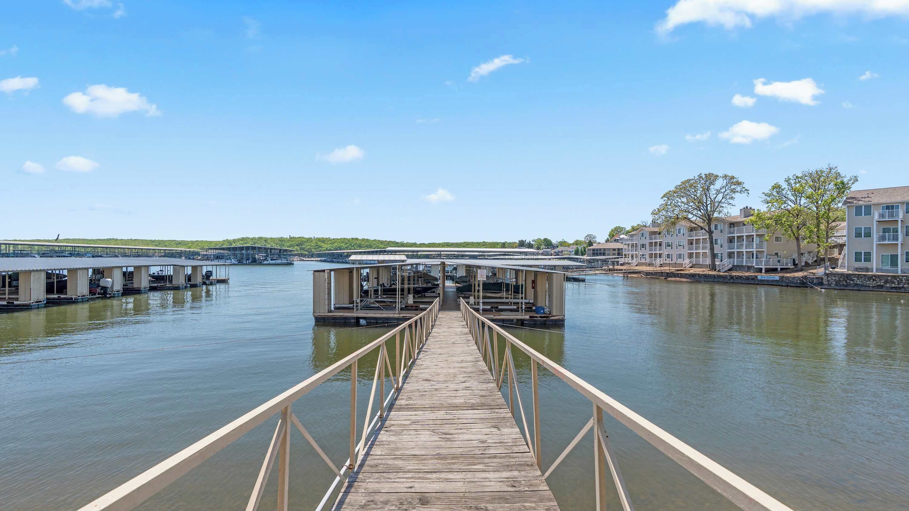 Un muelle de madera que conduce a estructuras flotantes, con vista a un río y edificios al fondo.
