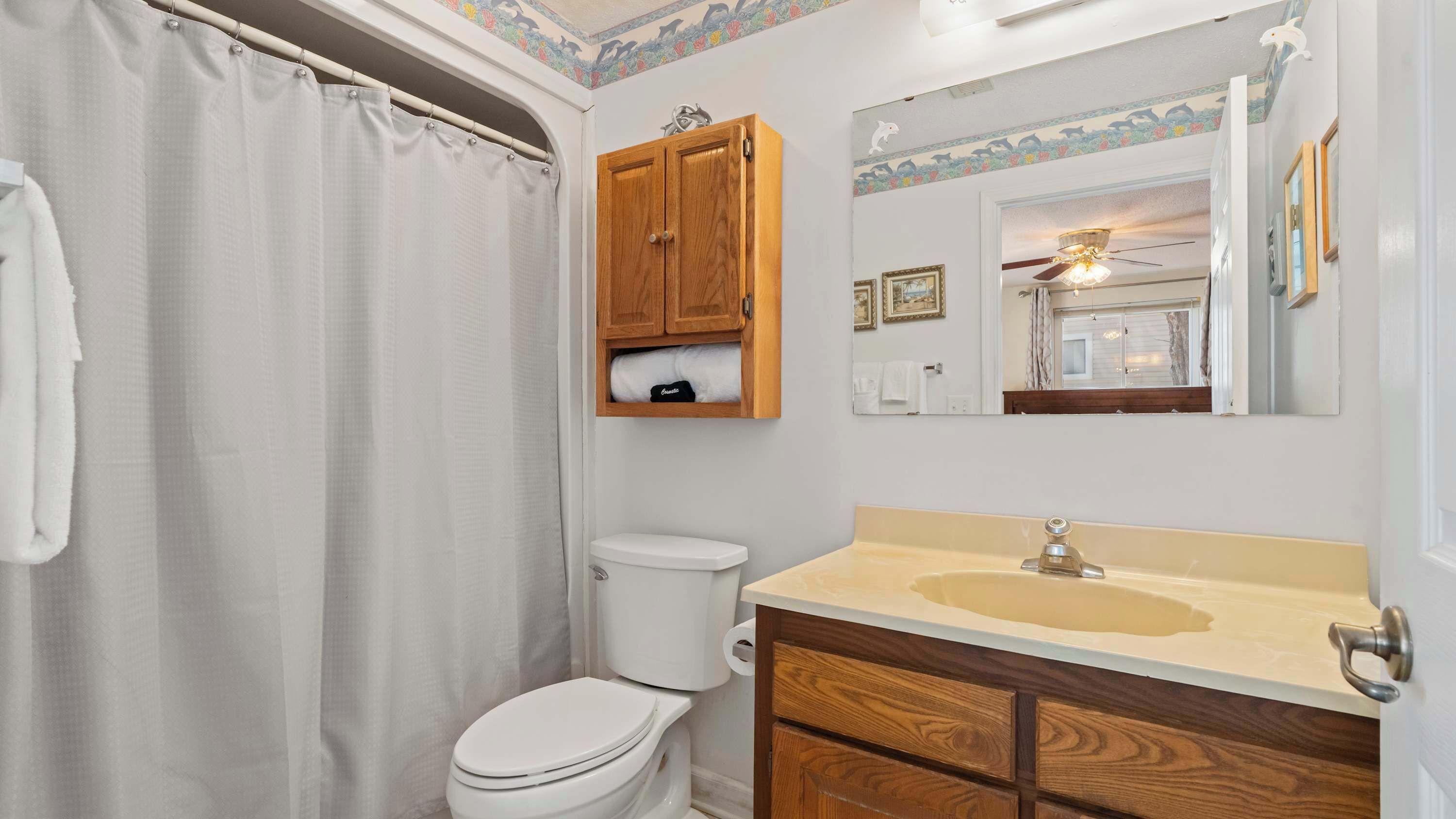 A bathroom with a shower curtain, toilet, wooden cabinet, vanity with a sink, and a mirror.