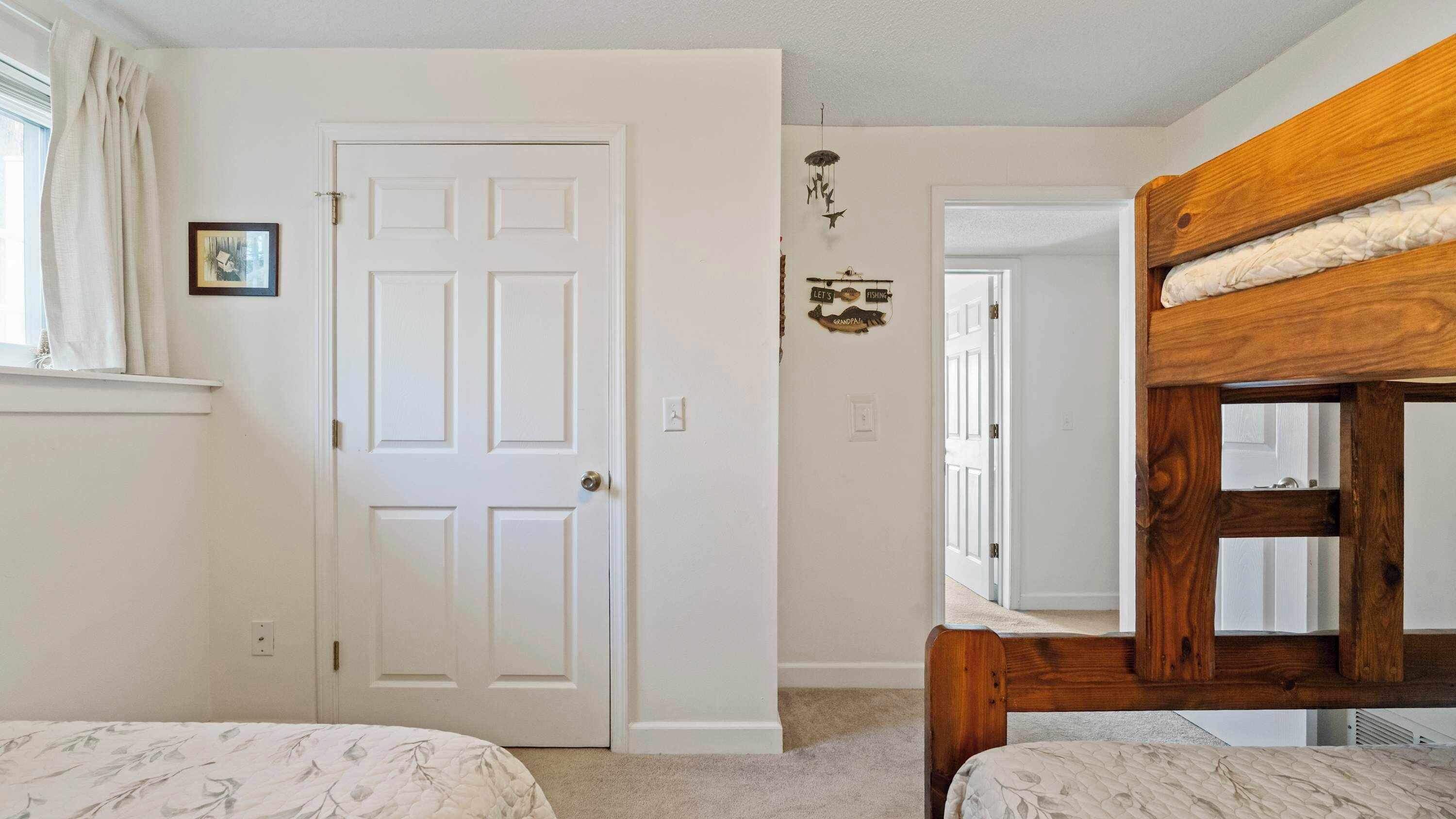 A bedroom with two beds, a white door, a small picture on the wall, and a wooden bunk bed.