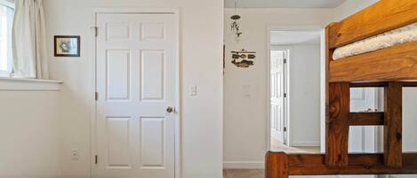 A bedroom with two beds, a white door, a small picture on the wall, and a wooden bunk bed.