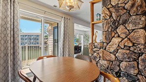 A dining area with a stone wall, a wooden table, and a view of a building through glass doors. - Ozark Get-away Lakefront Condo With Boat Slip (Osage Beach)
