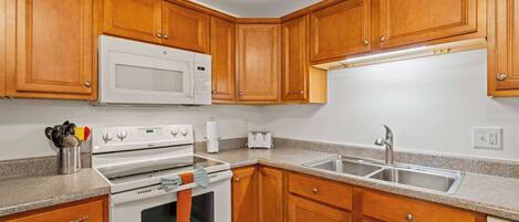 A kitchen with wooden cabinets, a white microwave, a stove, a sink, and a toaster.