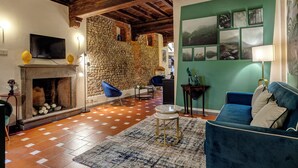 Ein Wohnzimmer mit Steinwand, Kamin, Fernseher, blauem Sofa und einer grünen Wand mit Bildern.