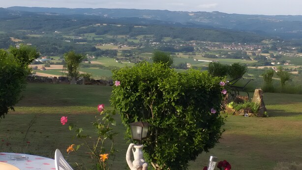 A garden with a white lamp post, a table with chairs, and a view of a rural landscape.