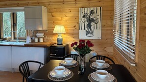 A wooden interior with a dining table set for four, a kitchen area, and a painting on the wall.