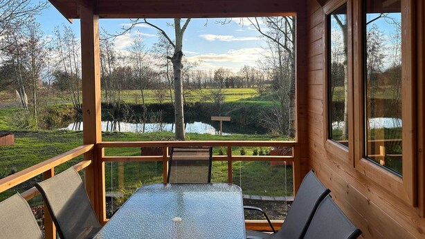 A wooden deck with a table and chairs, overlooking a pond and trees.