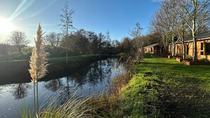 A serene lakeside setting with a wooden cabin structure, a grassy bank, and tall grasses along the water's edge.
