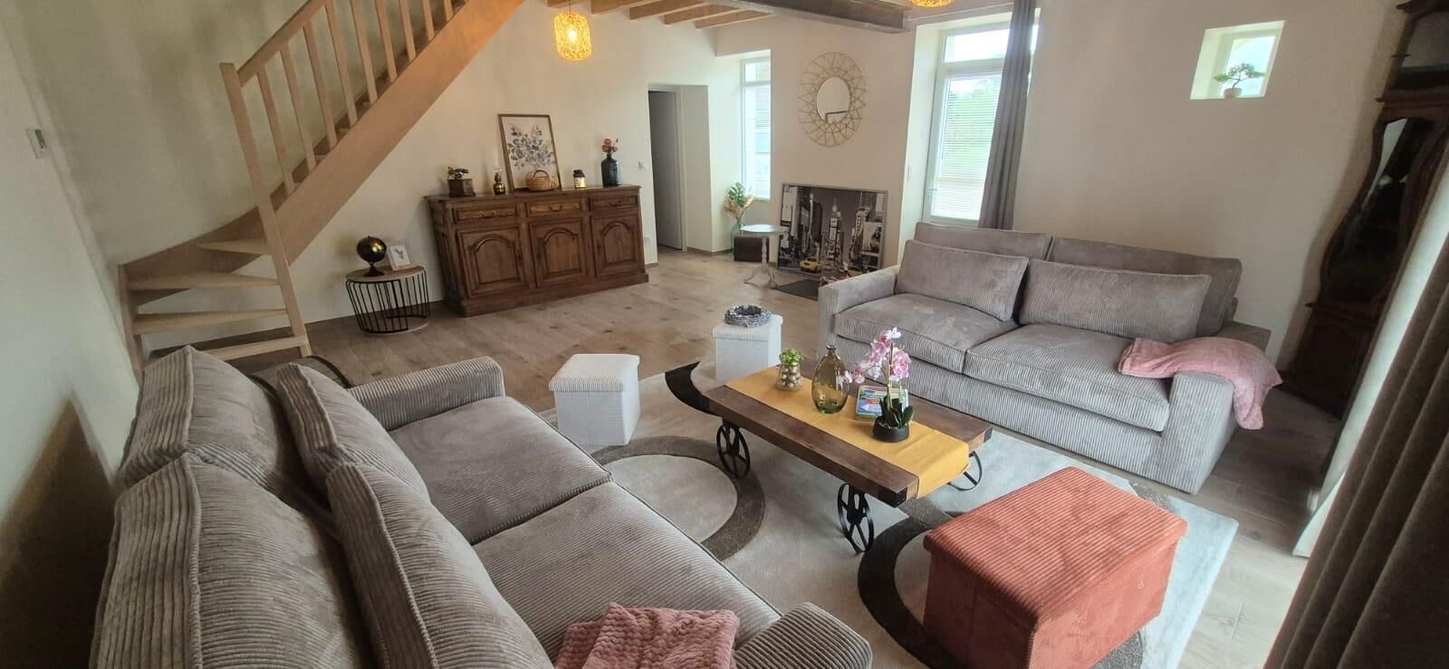 Ein geräumiges Wohnzimmer mit Treppe, einer Sofagarnitur, einem Couchtisch mit Dekoration und einem Kamin.