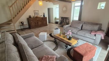 Ein geräumiges Wohnzimmer mit Treppe, einer Sofagarnitur, einem Couchtisch mit Dekoration und einem Kamin.