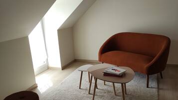 Een moderne loft slaapkamer met een schuin dak, een bruine fauteuil, een klein tafeltje met boeken en een witte vloerkleed.