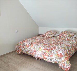 Een slaapkamer met een schuine plafond, een bloemenbedekker en een houten vloer.