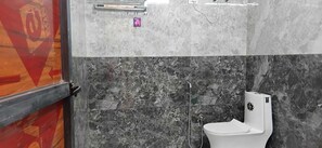A bathroom with a white toilet, a shower, and a marble wall. - Bohara Bhawan (Jaipur)