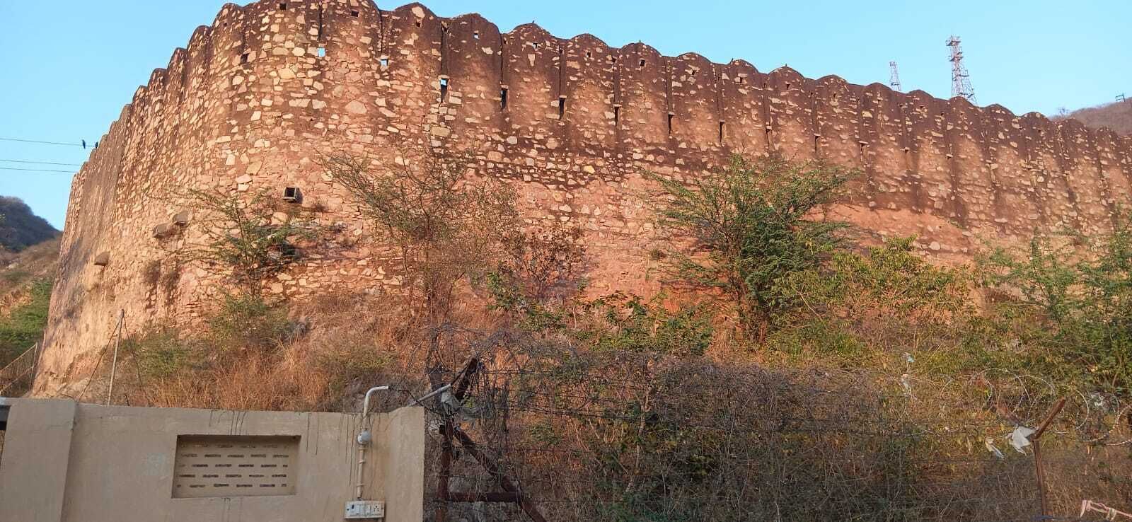 Um grande muro de pedra antiga, com uma série de aberturas, rodeado por vegetação rala.