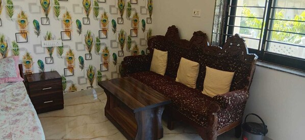 A room with a sofa set, a small table, a cabinet, and a window with a view of greenery. - Bohara Bhawan (Jaipur)