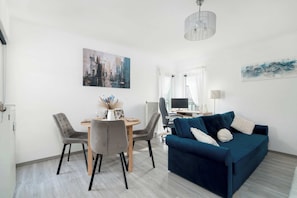 Un salon moderne avec un canapé bleu, des fauteuils gris, une table à manger et des œuvres d’art accrochées aux murs.