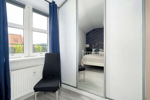 Une chambre à coucher avec un lit, une chaise, une fenêtre avec des rideaux et une vue sur les bâtiments à l’extérieur.