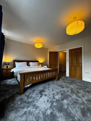 A bedroom with a wooden bed, two bedside lamps, a ceiling light, and a door leading to another room. - Cosy Buxton Terraced House (Buxton)