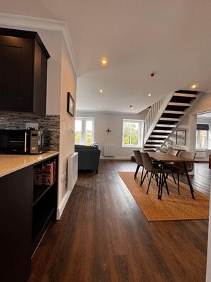A modern kitchen with dark cabinets, a built-in microwave, and a wooden countertop. There is a dining area with a table and chairs, and a staircase leading to an upper level. - Gorgeous Spacious Buxton Park Apartment (Buxton)