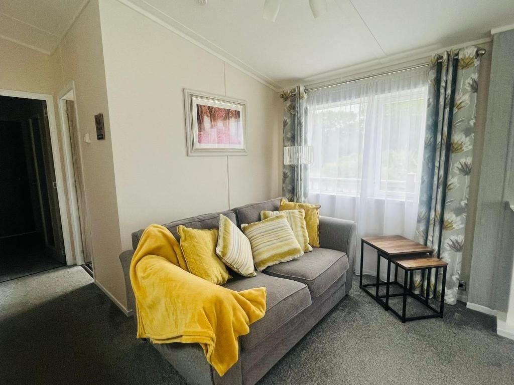 Un salon avec un canapé gris, des plaids jaunes, une petite table en bois et un tableau encadré au mur.
