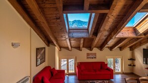 Un salon spacieux avec des poutres apparentes, un canapé rouge et une vue sur les montagnes grâce à des fenêtres de toit.