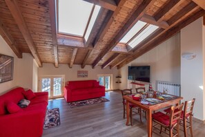 A spacious living area with a red sofa, wooden dining table, and a TV.