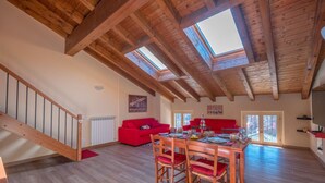 Un loft spacieux avec des poutres en bois, un coin repas avec des chaises rouges et un canapé rouge.