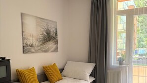 Un dormitorio con cama, mesita de noche, cómoda, ventana con cortinas y un cuadro en la pared.
