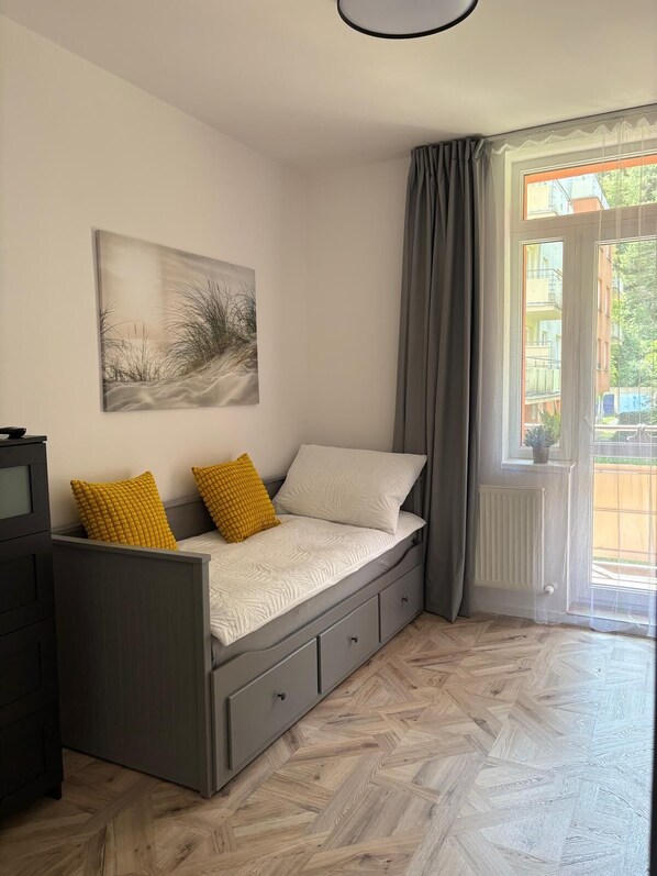 Un dormitorio con cama, mesita de noche, cómoda, ventana con cortinas y un cuadro en la pared.