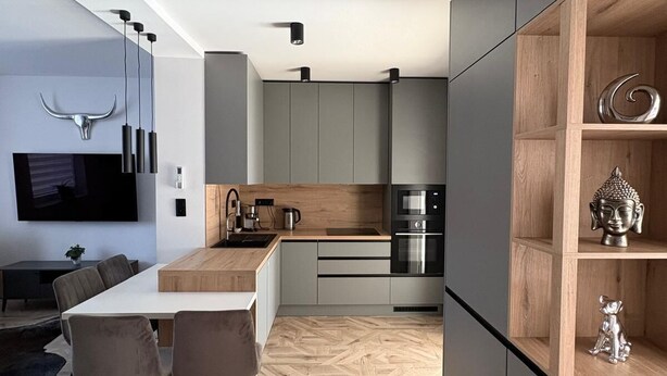 Una cocina moderna con suelo de madera en patrón de espiga, electrodomésticos integrados y una zona de comedor con mesa y sillas en el mismo diseño.