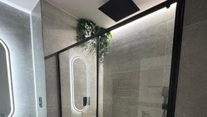 Un baño moderno con ducha de vidrio, tocador de madera con un lavamanos grande y un espejo con marco circular.